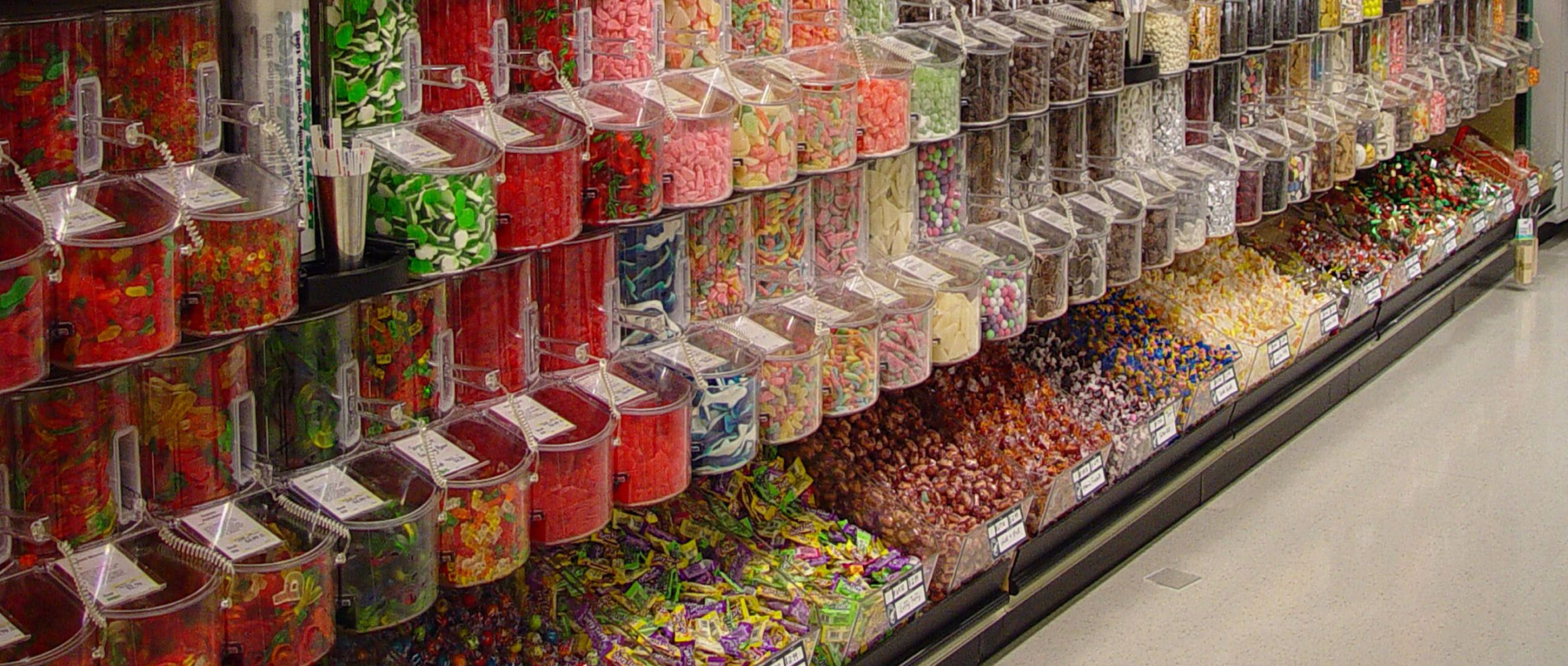 A photo of a store aisle with candy filled gravity bins.